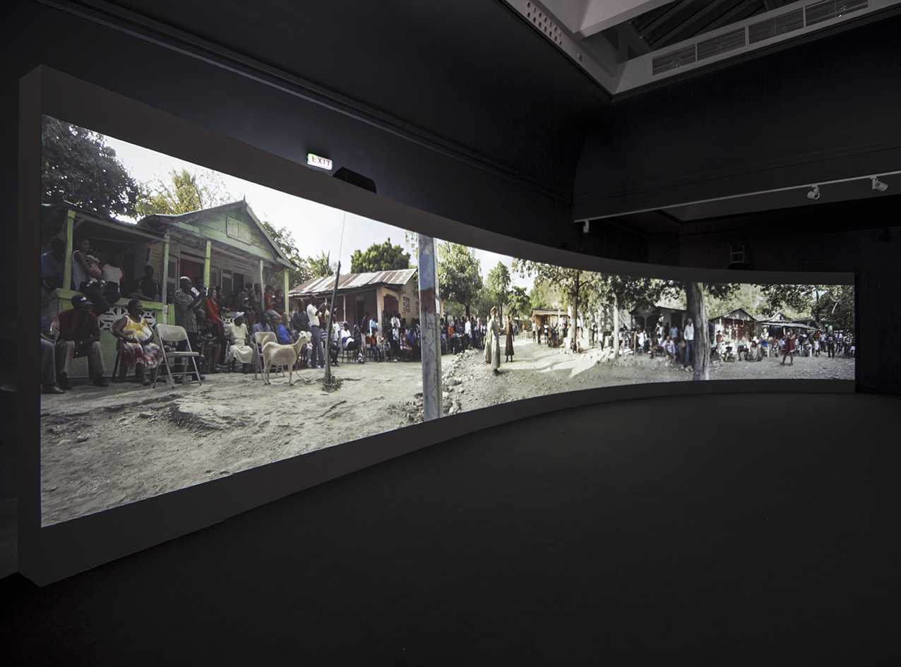 A long curved projection of a video depicting a building with people gathered in front