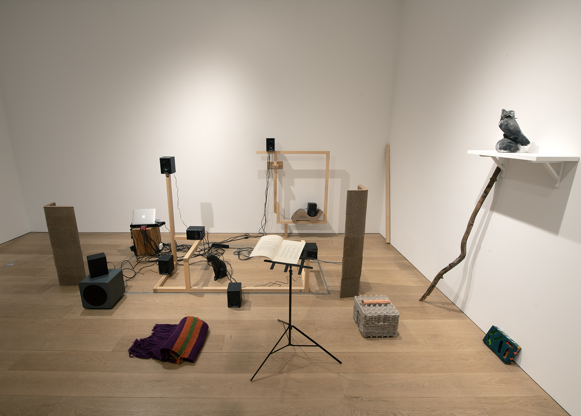 Wooden framework supports speakers with a scarf, a music stand, and raw materials arranged on the ground surrounding the framework