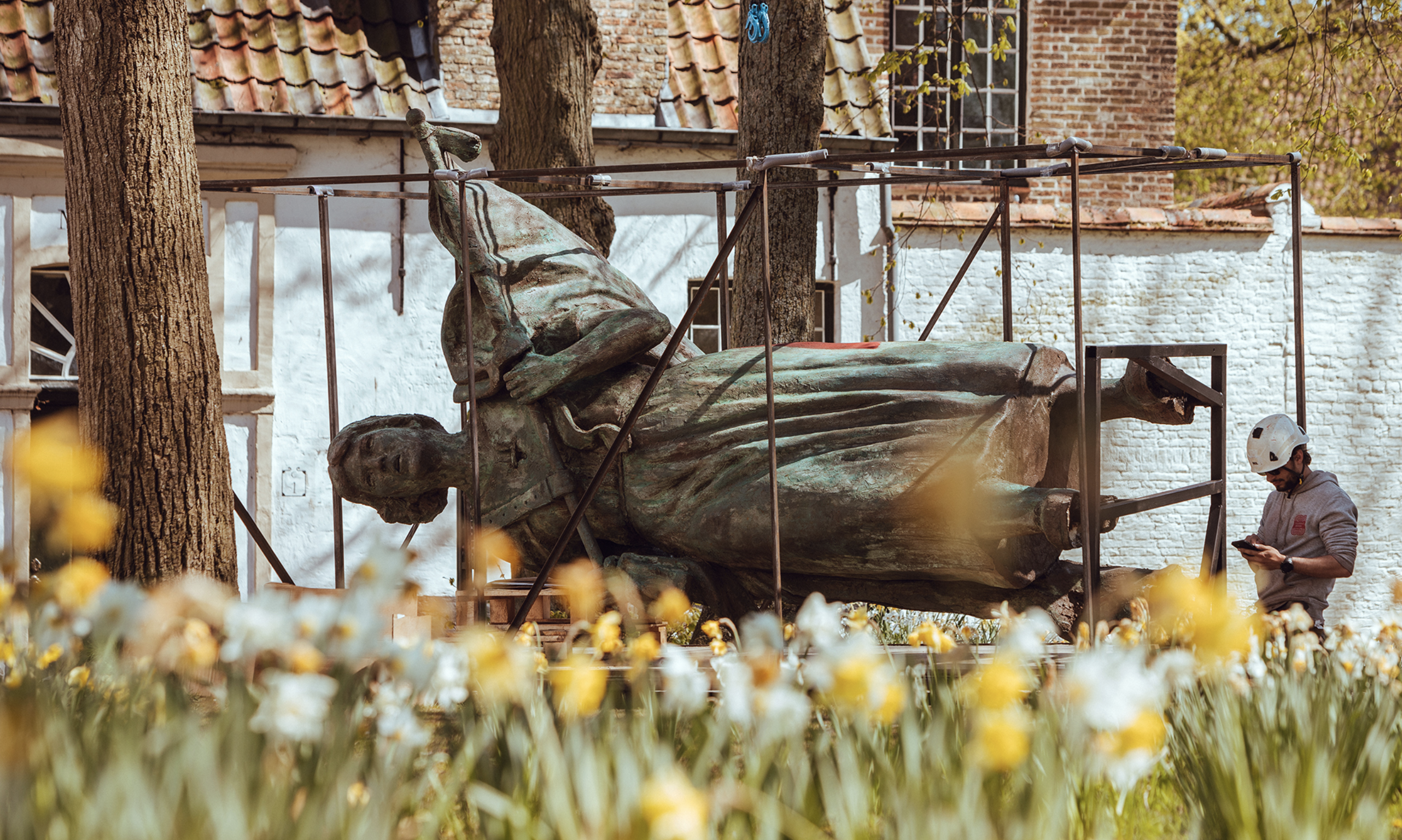 Statue of a person is positioned horizontally on the ground with tulips in the foreground