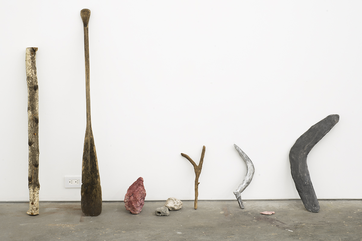 Wooden and stone implements are arranged on the floor leaning against a white wall