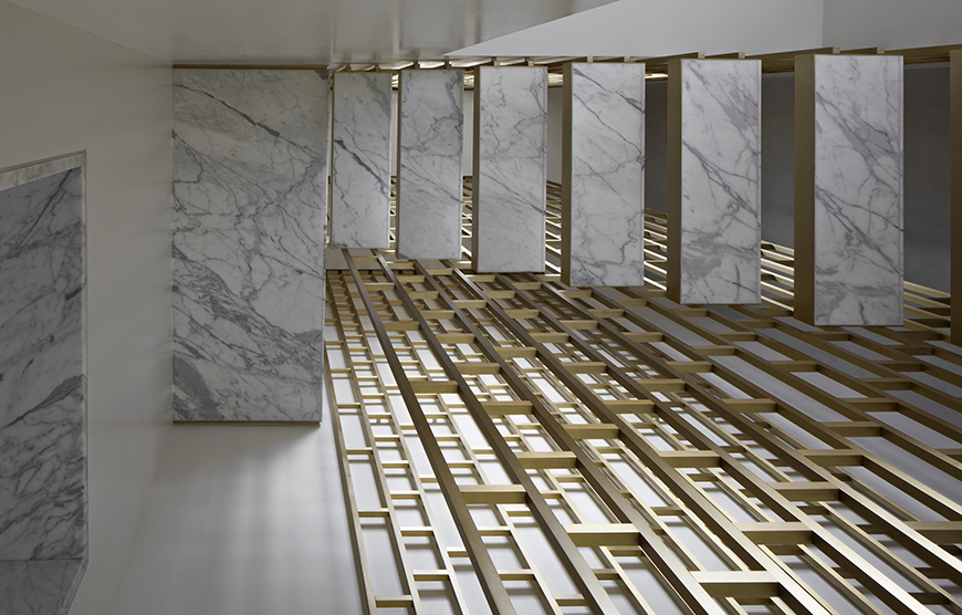 White and gray marble slabs are positioned vertically in a room with grids of wood flooring below.