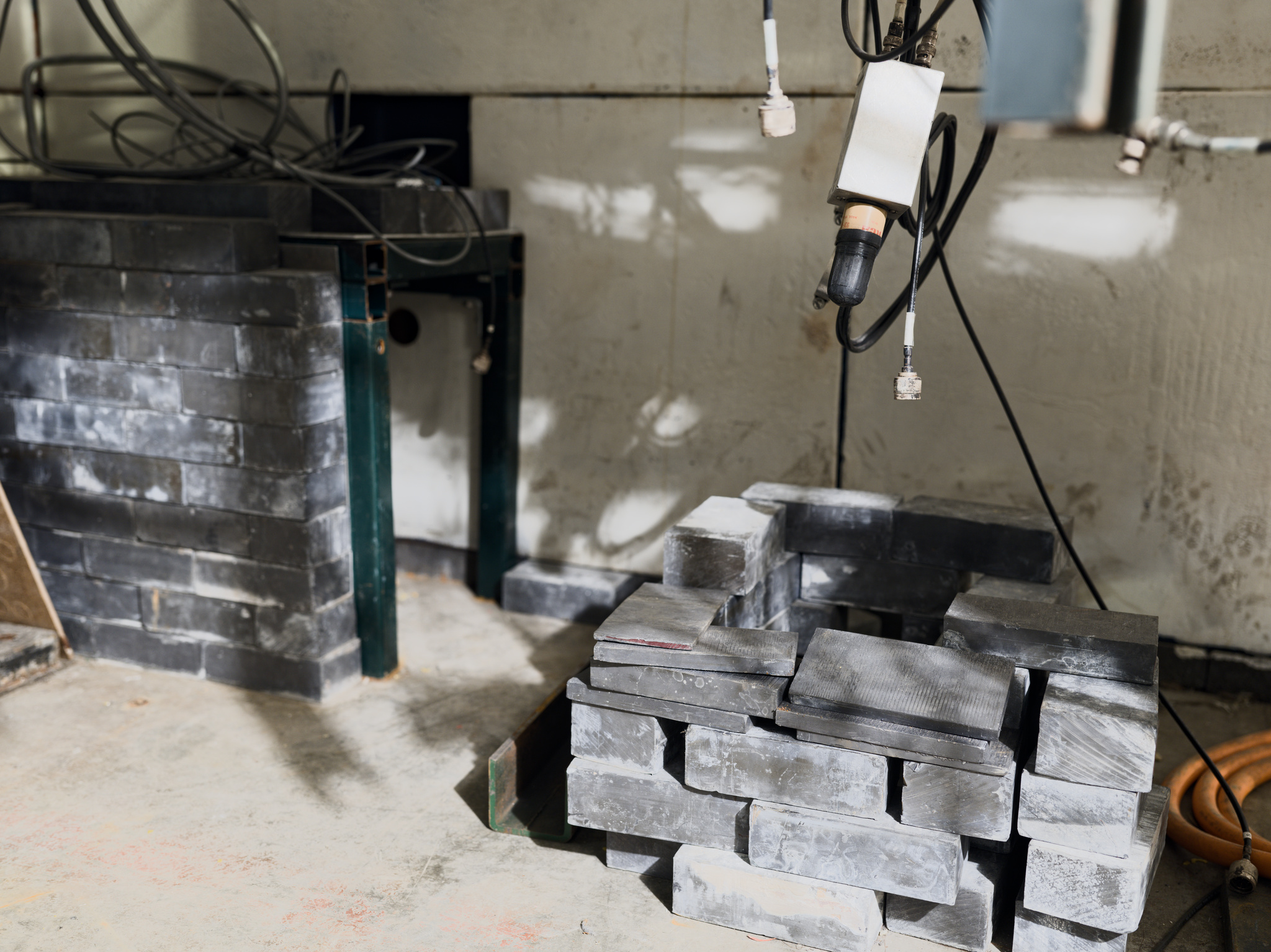 Concrete bricks loosely stacked beneath black cables that hang from ceiling
