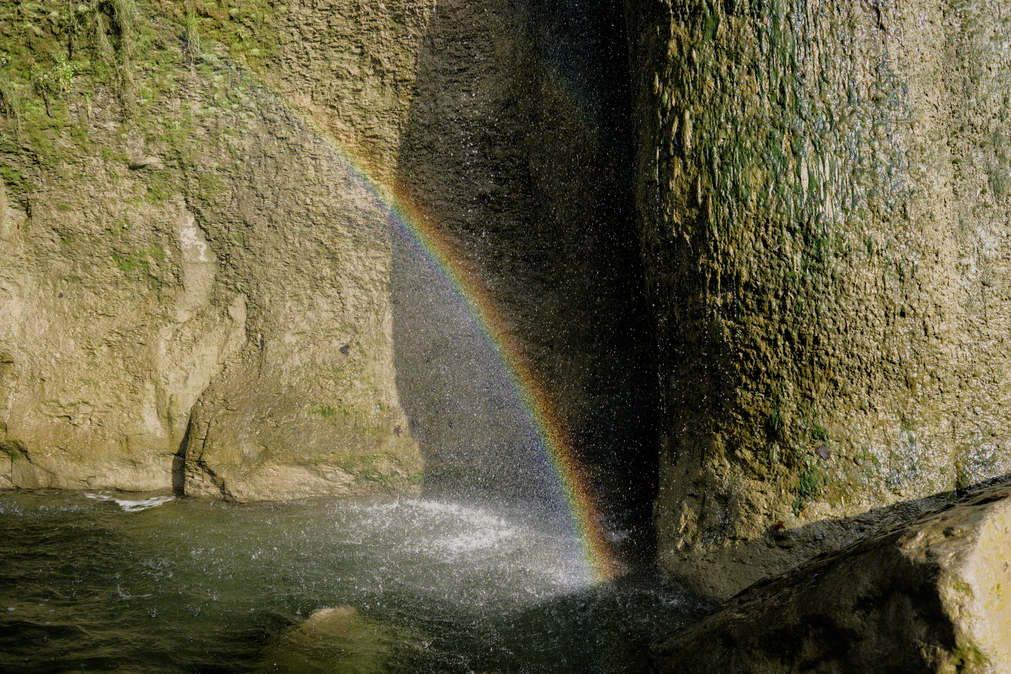 Rock wall with water in the foreground and a rainbow above the water