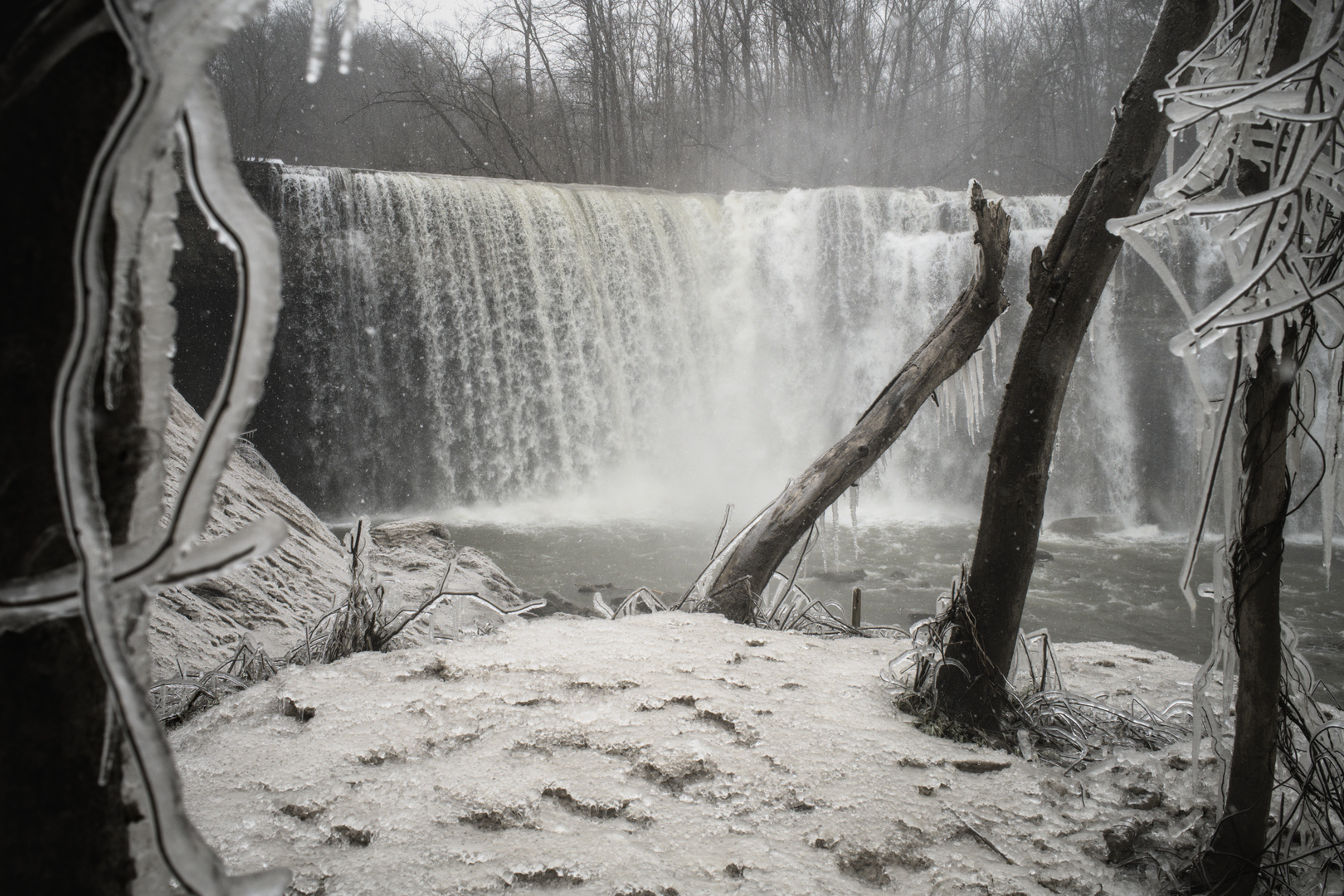 Waterfall in the background during the winter time with an icy snow covered patch of grass in the foreground