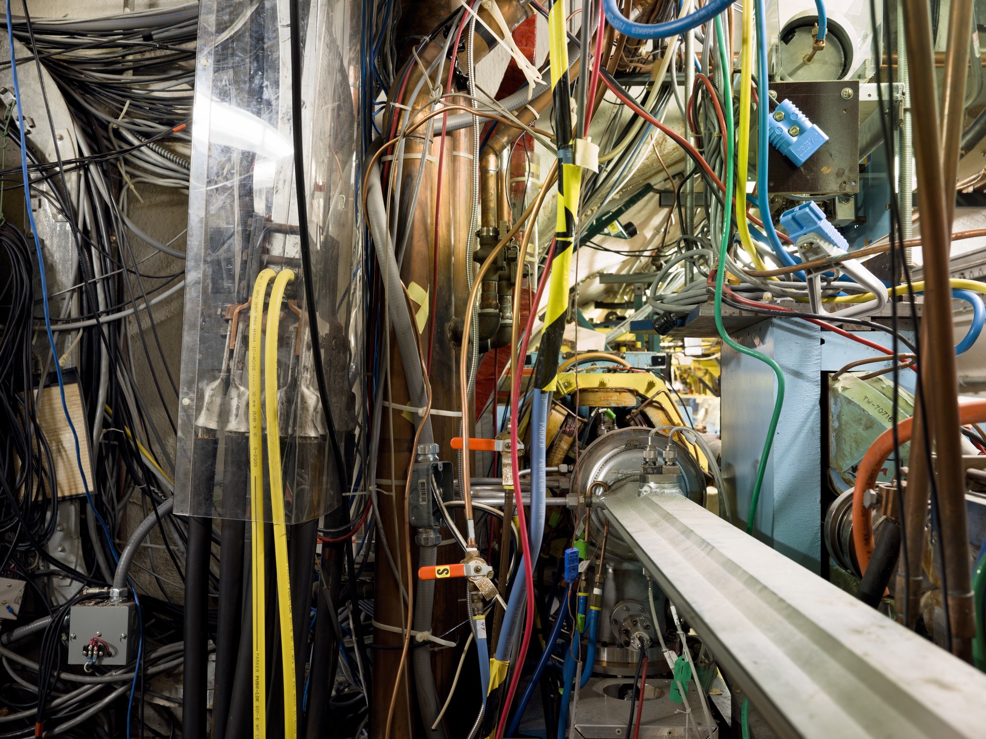A convergence of multi colored cables plugged into a wall with metal support structures throughout