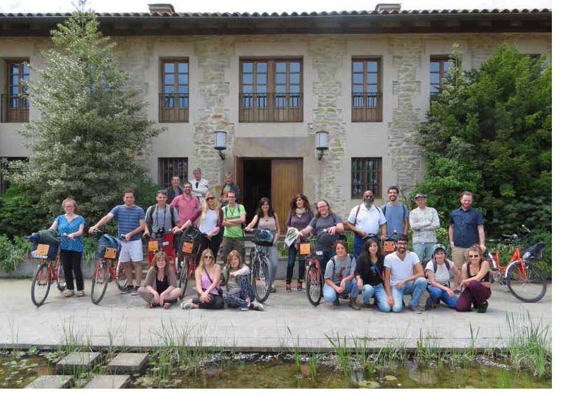 a group of people taking a photo in front of a building, many of them are holding bikes and some are kneeling