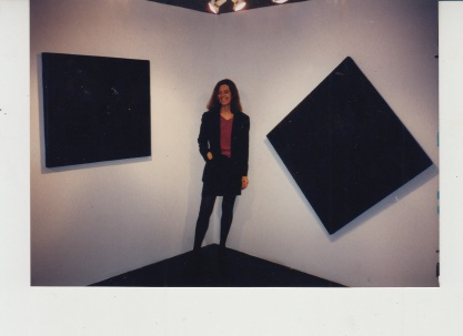 Pat Lipsky standing in between a square-shaped painting and a diamond-shaped painting at The Black Paintings (1998) exhibition in New York City.