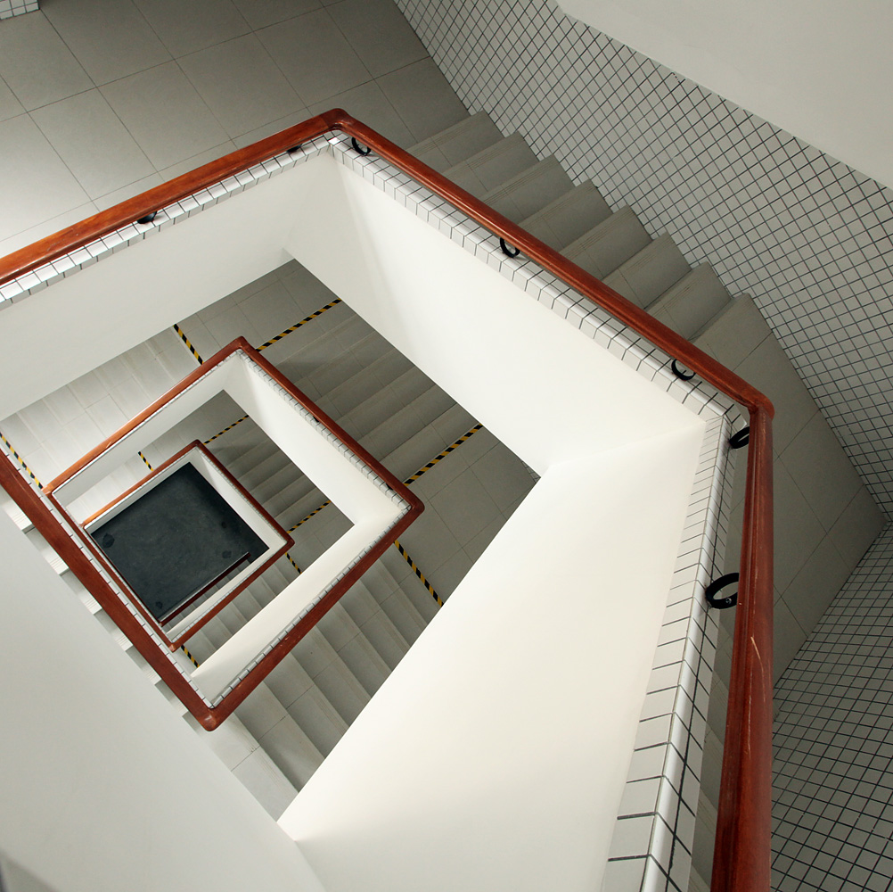 View of a rectangular stairwell with white walls and stairs and wooden railings.