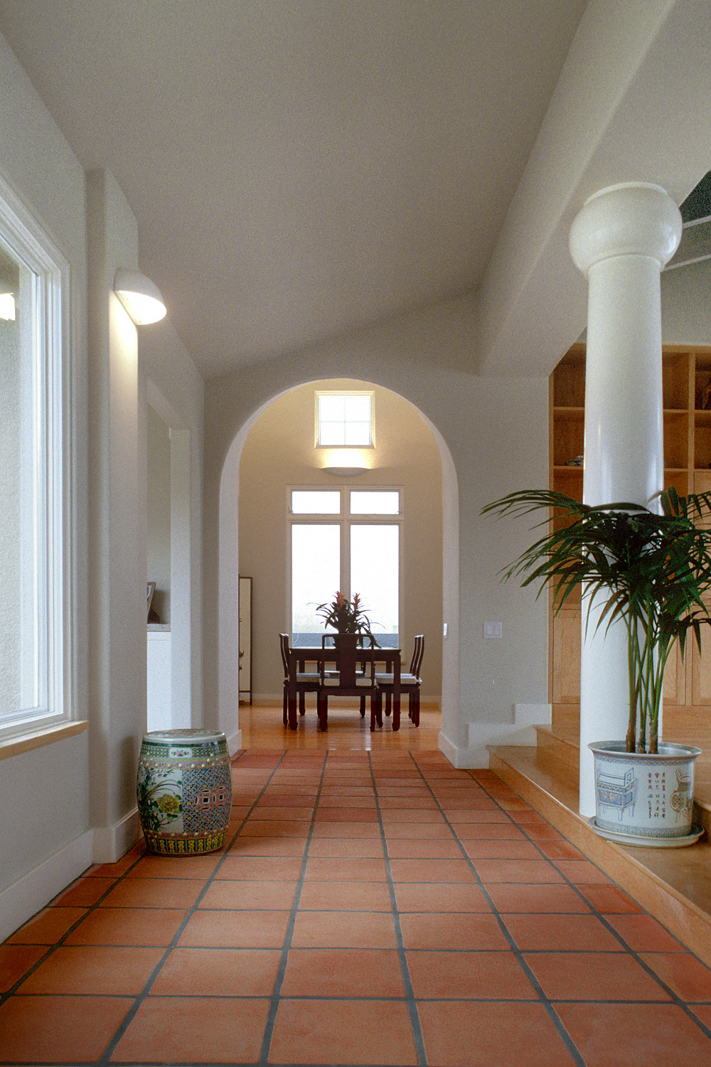 A hallway leads to a room with a table and chairs in front of a window.