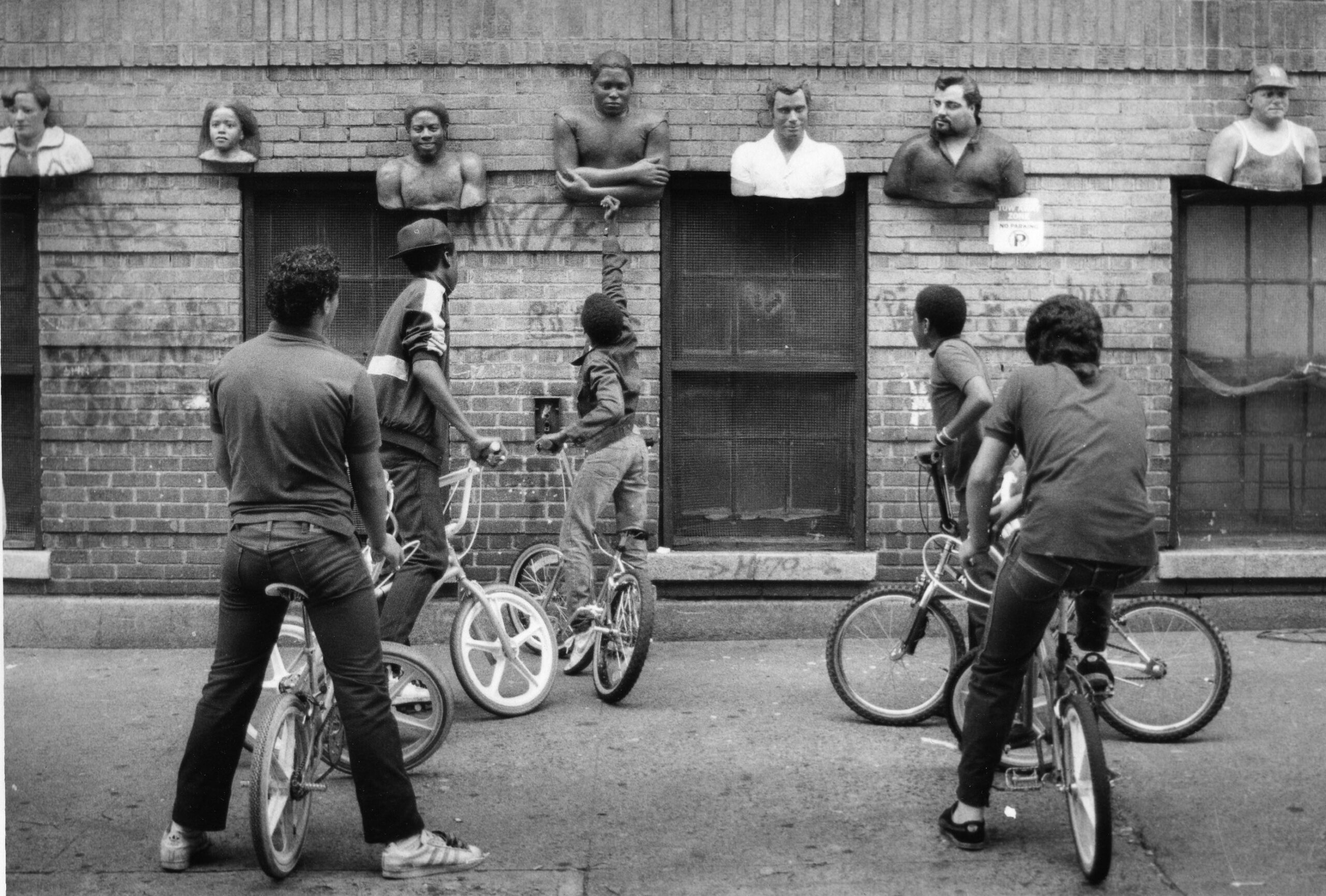 a black and white photo of kids on bikes in front of sculpture reliefs hanging outside on a building