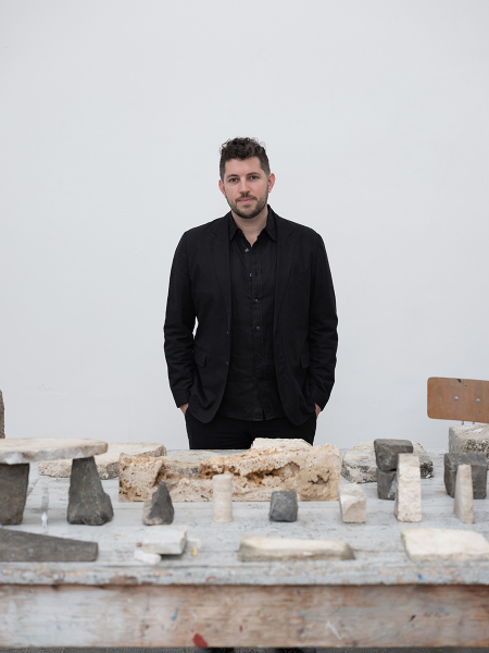 Person wearing black clothing stands behind a table with building materials on display.
