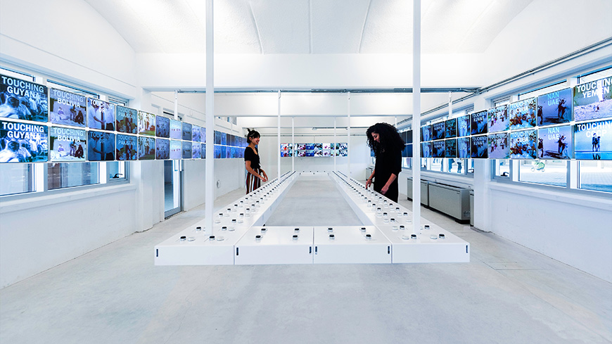 The modern interior of a building, whose walls are primarily white and overlaid with rows of television screens.