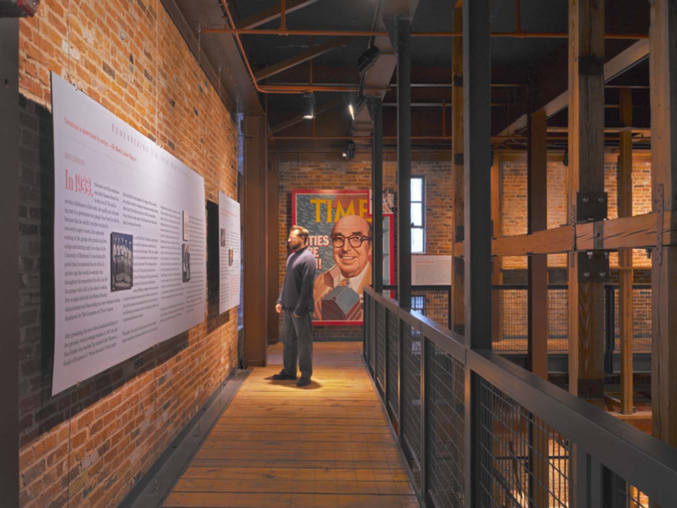 A man reads large prints installed on a brick wall