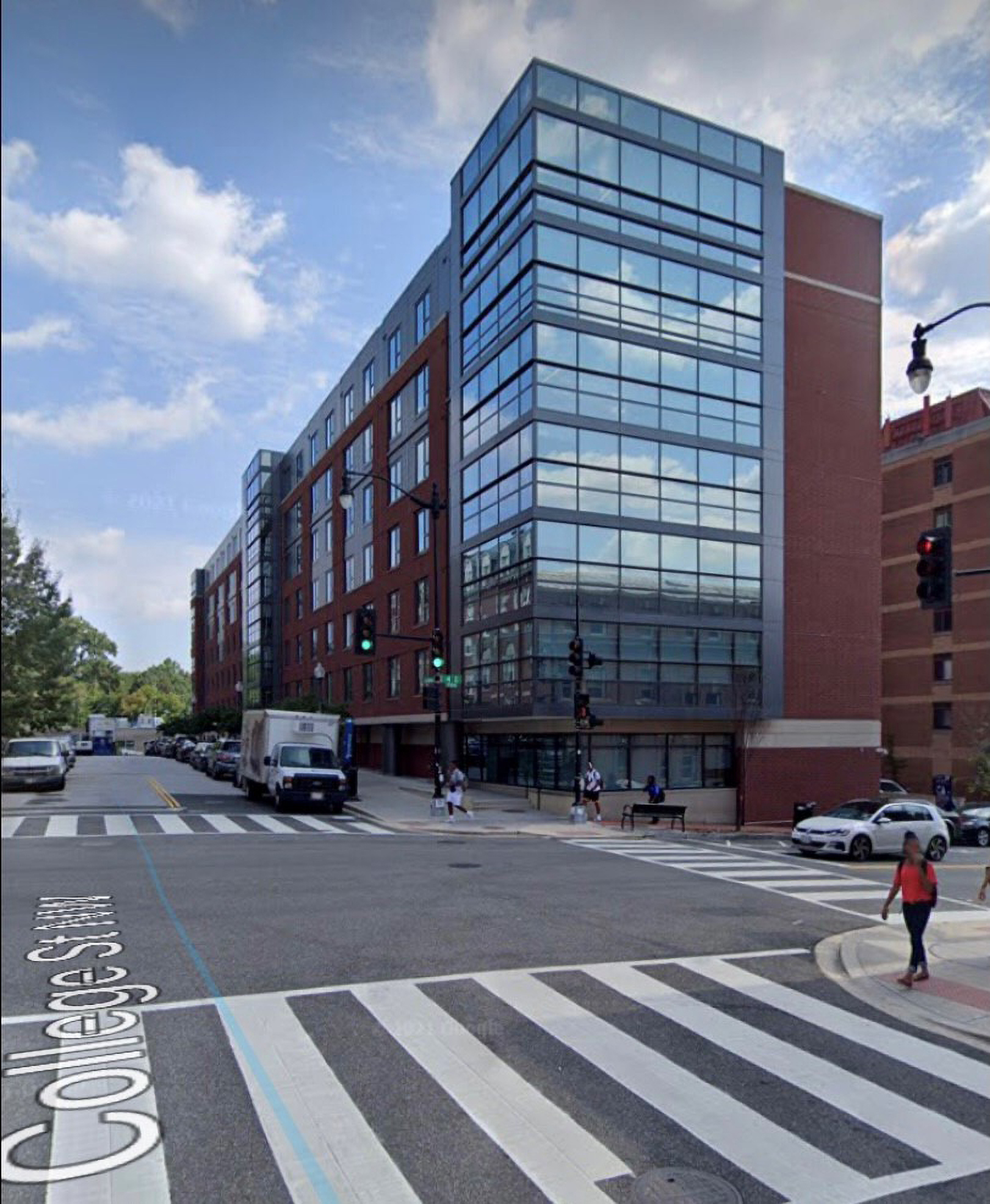 A glass-walled corner of a building reflects the blue sky and clouds.