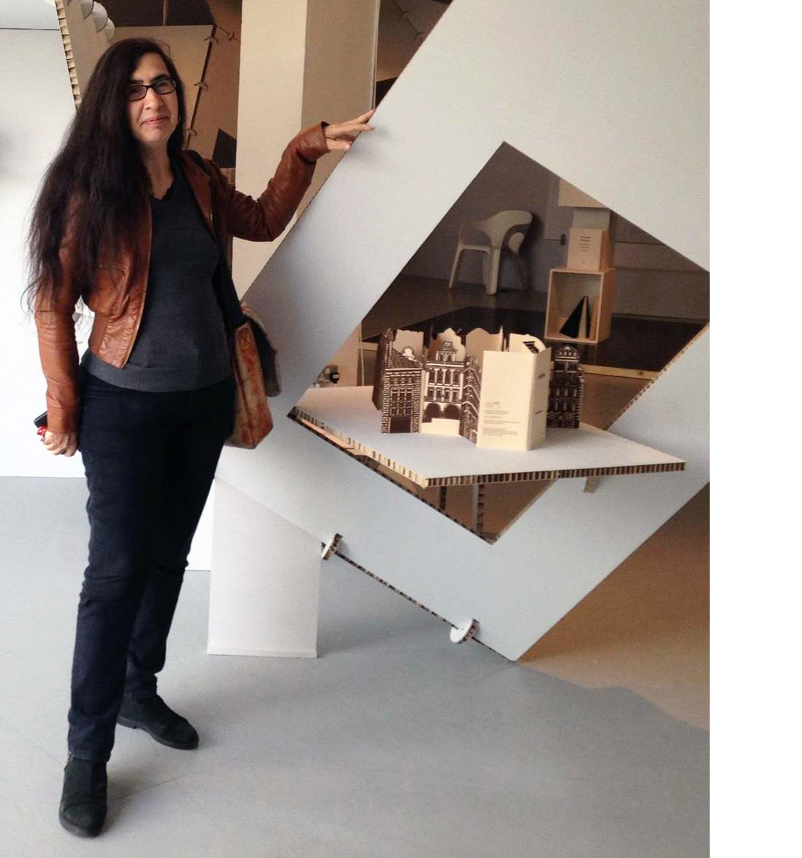 A woman with long brown hair holds up a thick piece of white cardboard with a large rectangle cut out of it, resembling a frame.