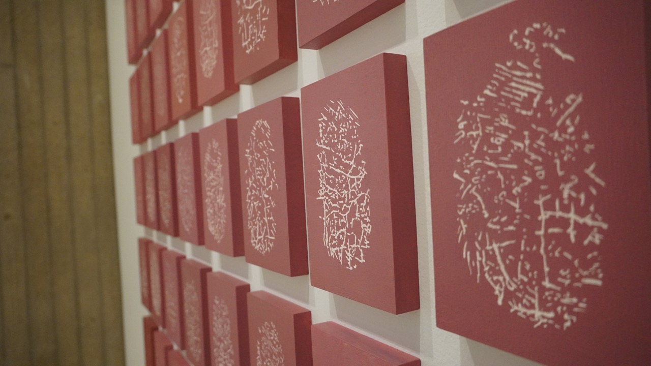 Detailed view of terracotta colored abstract prints in a grid format on gallery wall