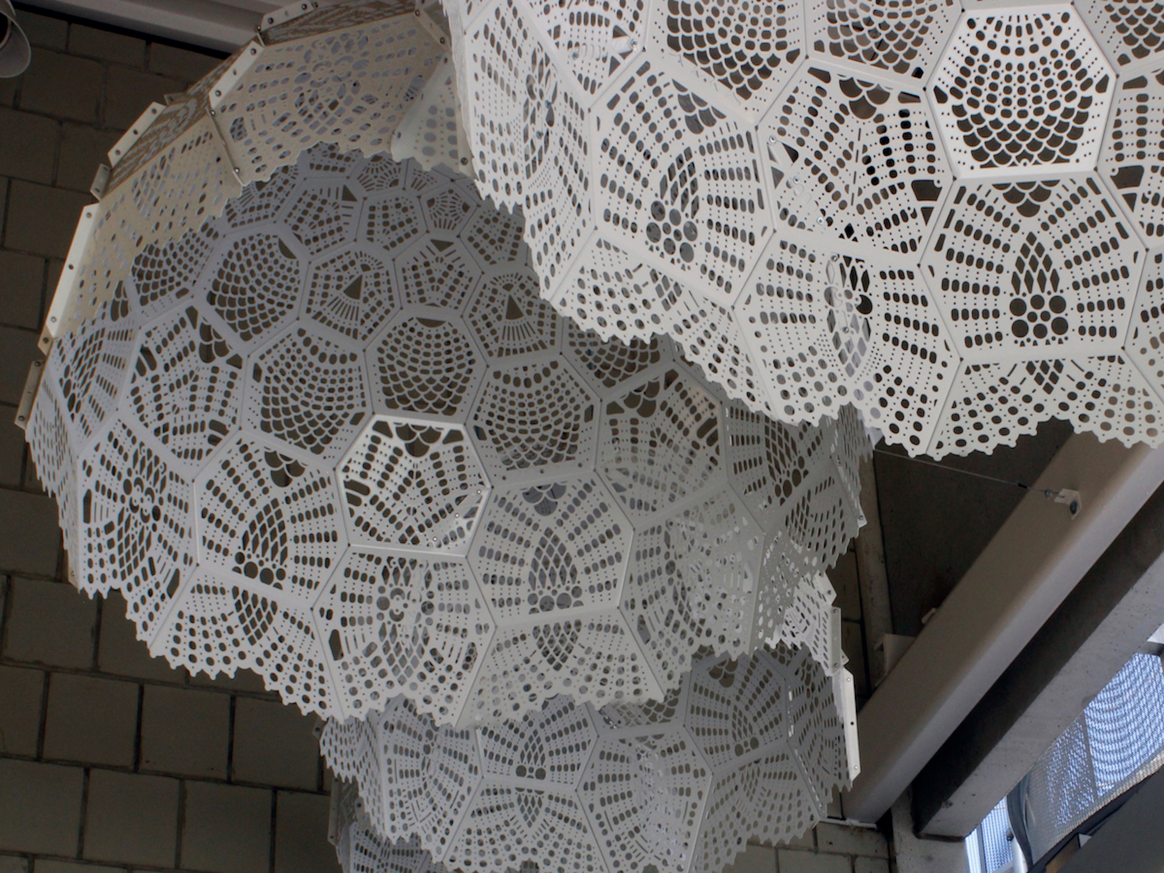 Closeup view of large white doily sculptures hanging from a ceiling.