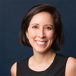 headshot of smiling woman in black with a dark blue back drop. 