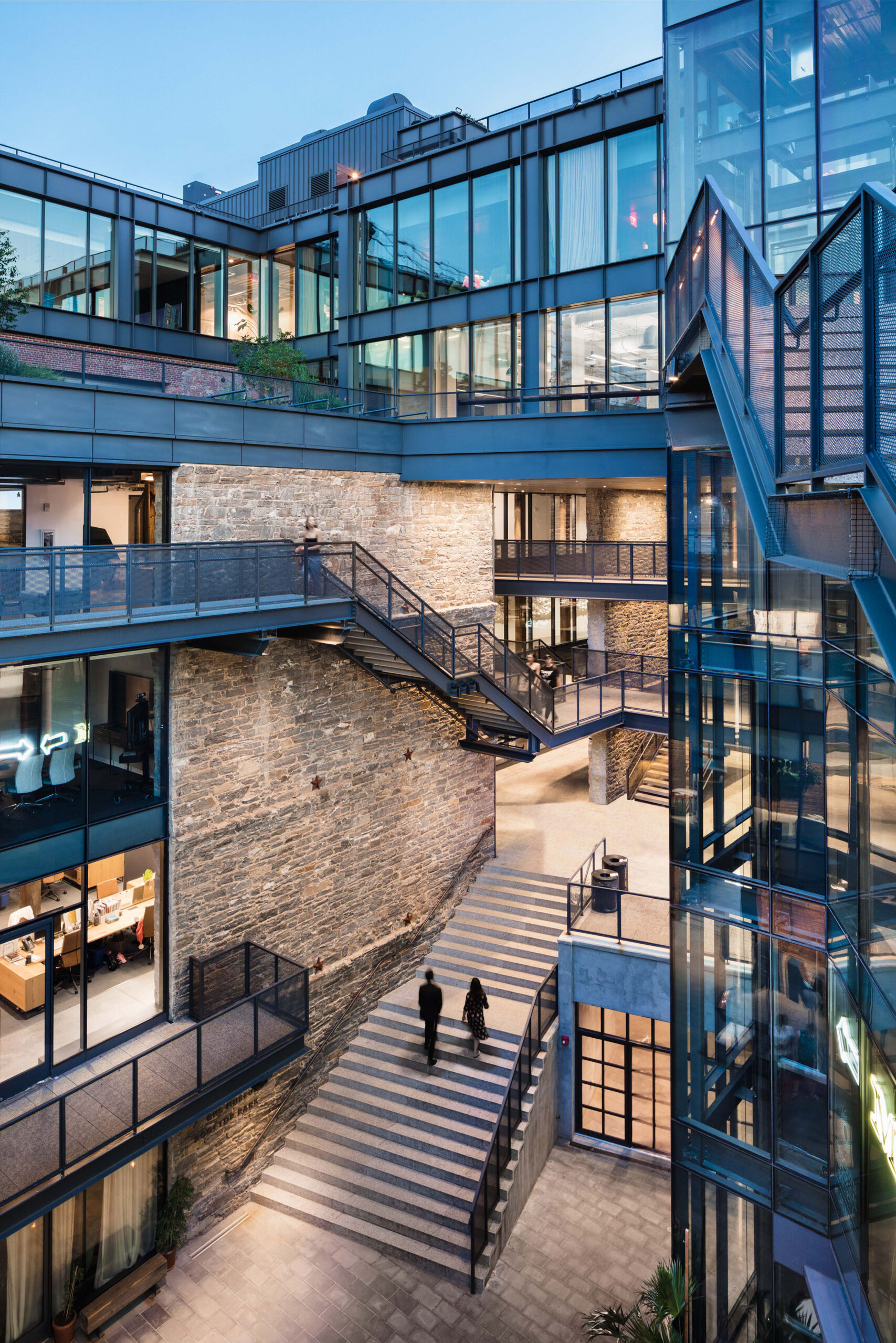 A skywalk connects the top floors of two buildings. Exterior stairs wind around the buildings.