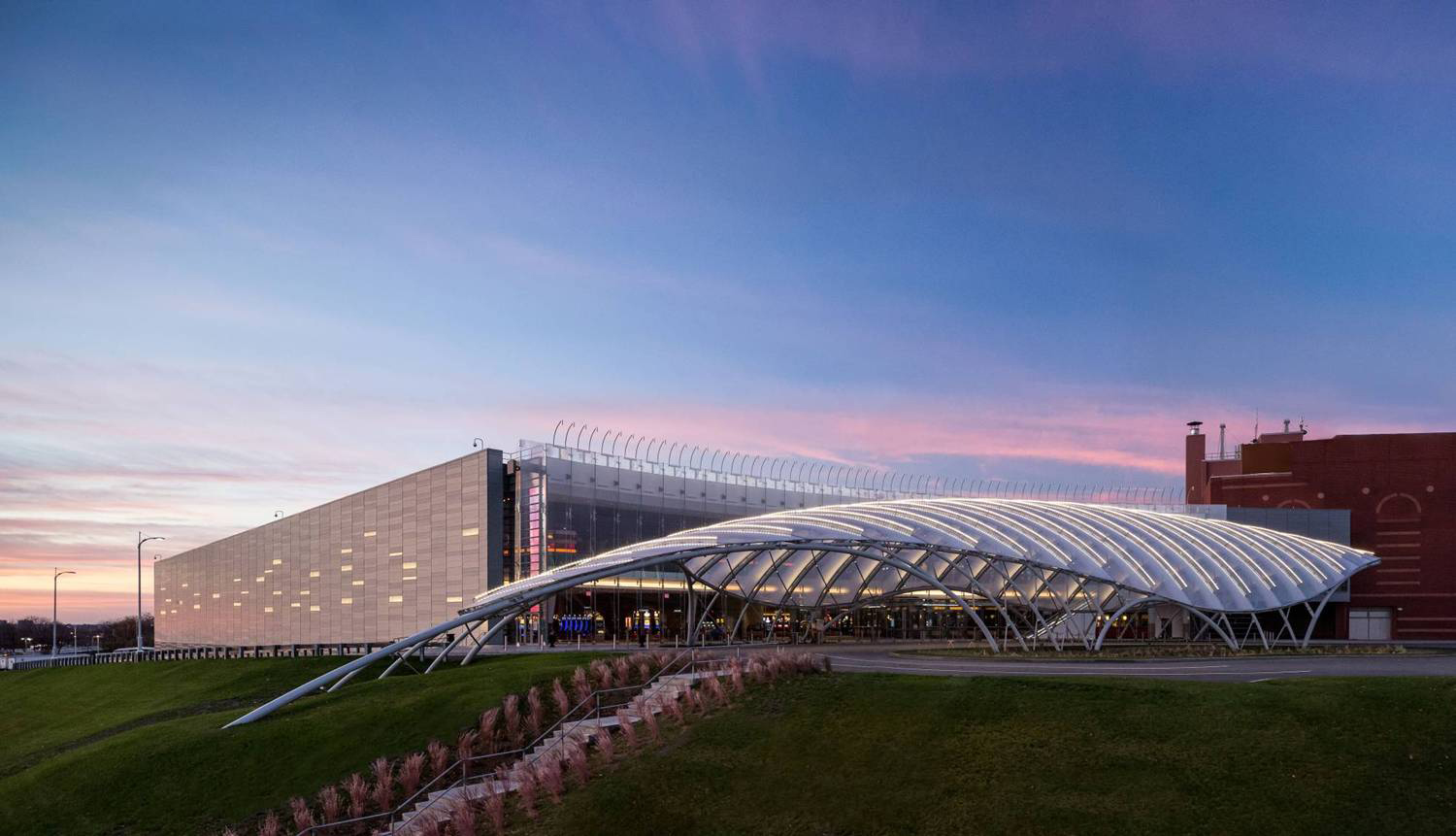 Hillside stairs lead up to a steel grid-shell of perforated zinc and curved facade of suspended glass.