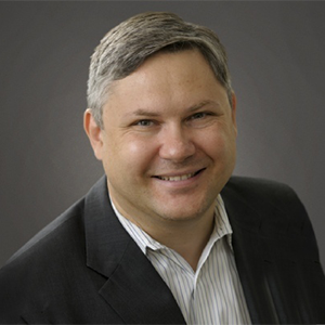 Man wearing a dark suit jacket and white collared shirt.