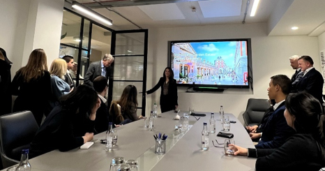 people around a table looking at a screen and a person speaking