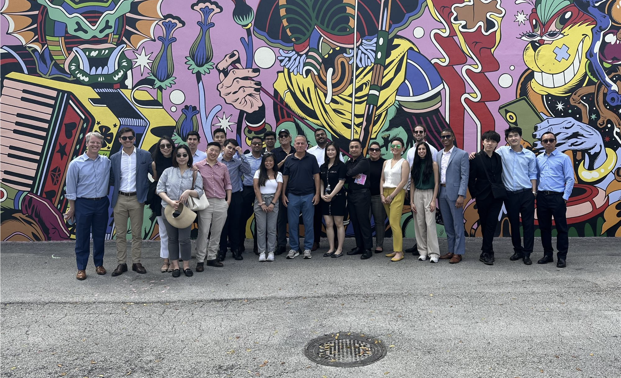 Large group of people posing in front of a bright mural on an exterior building wall
