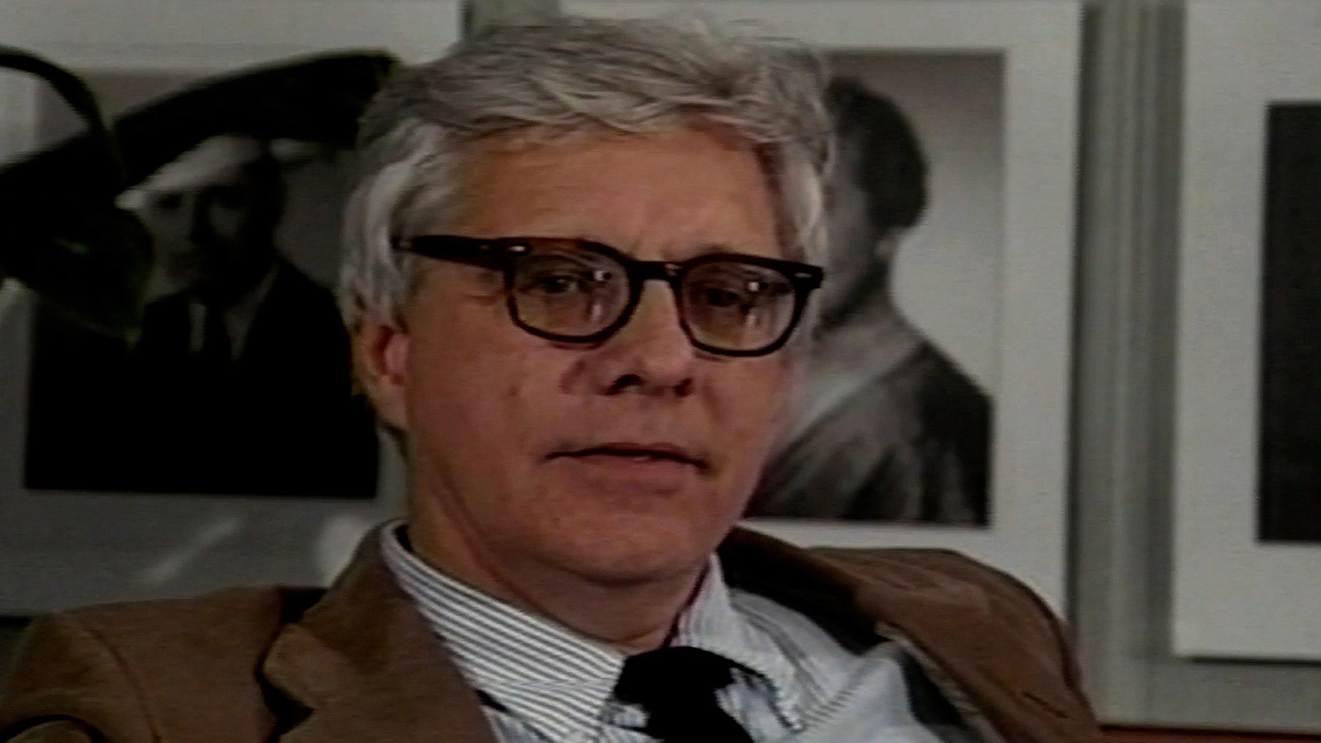 A man with a mix of gray and white hair, wearing glasses, and dressed professionally.