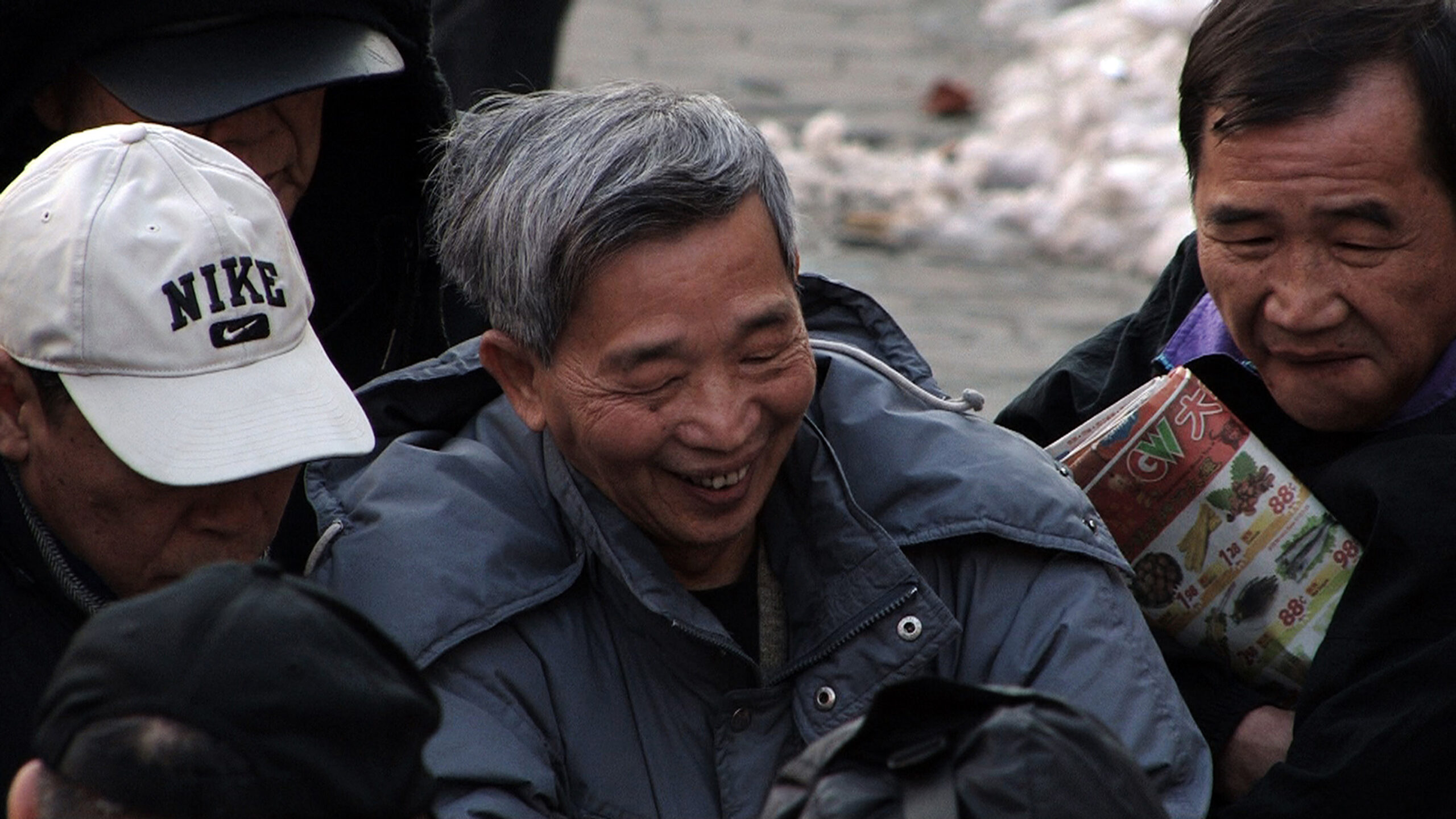 Three Chinese men huddle together outside, wearing winter coats.