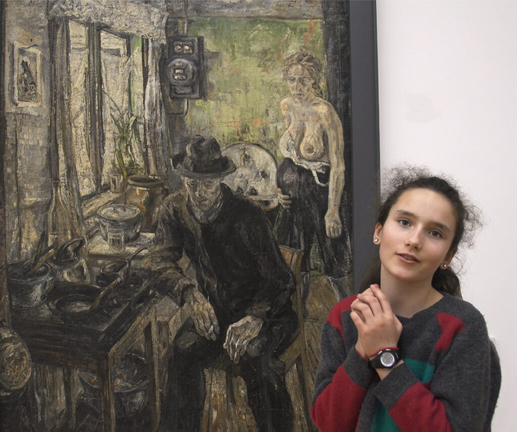 A teenage girl stands in front of a painting of a fully dressed man sitting and a half-naked pregnant woman standing in a residence.