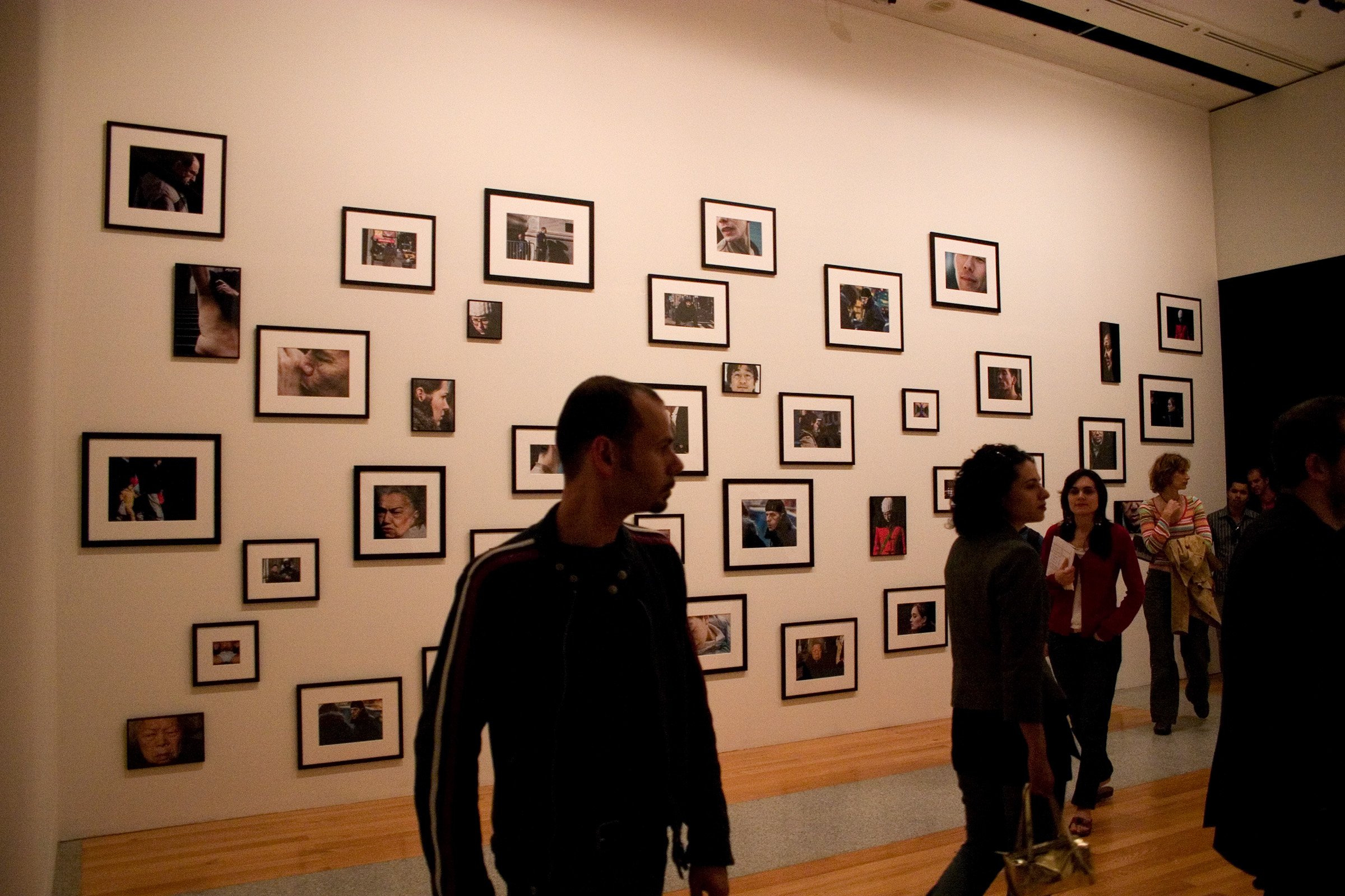 People mingle in a gallery. Framed photos cover the wall behind them.