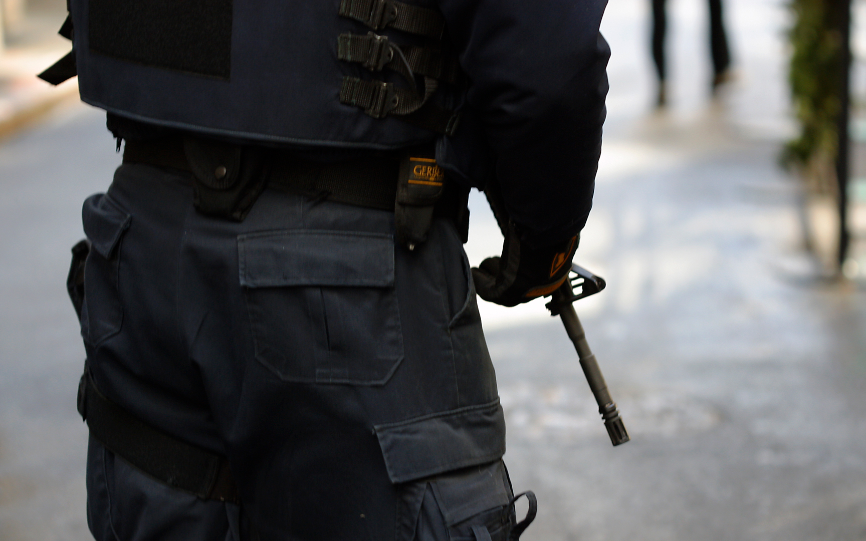 View of the back of a man's torso, clad in black tactical gear and holding a gun.
