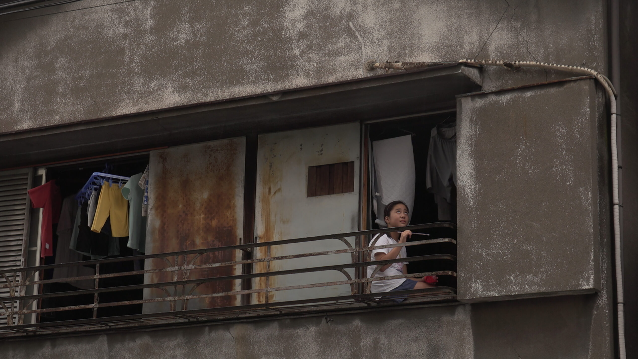 A young girl sits on a rusty balcony