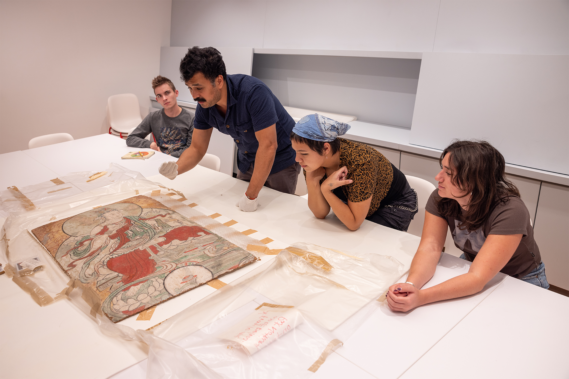 People gathered around a table looking at a piece of a fresco laid out on the table.
