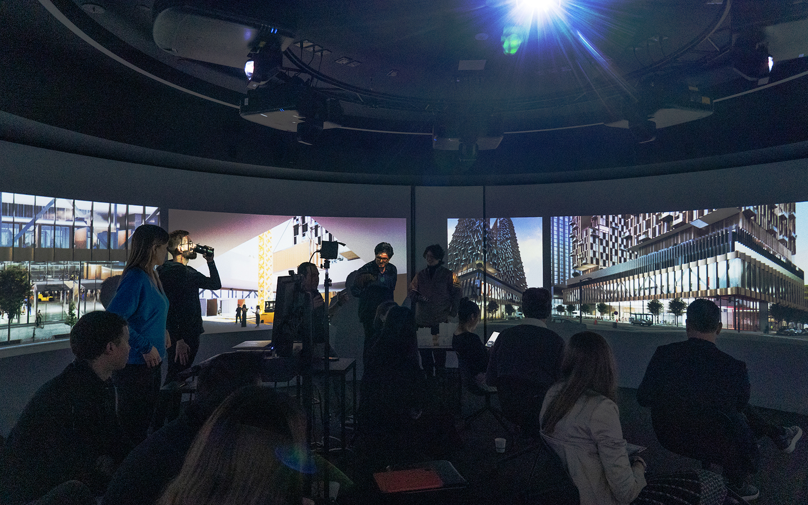 Students and faculty gathered in a darkened, high-tech conference room with wrap-around digital screens