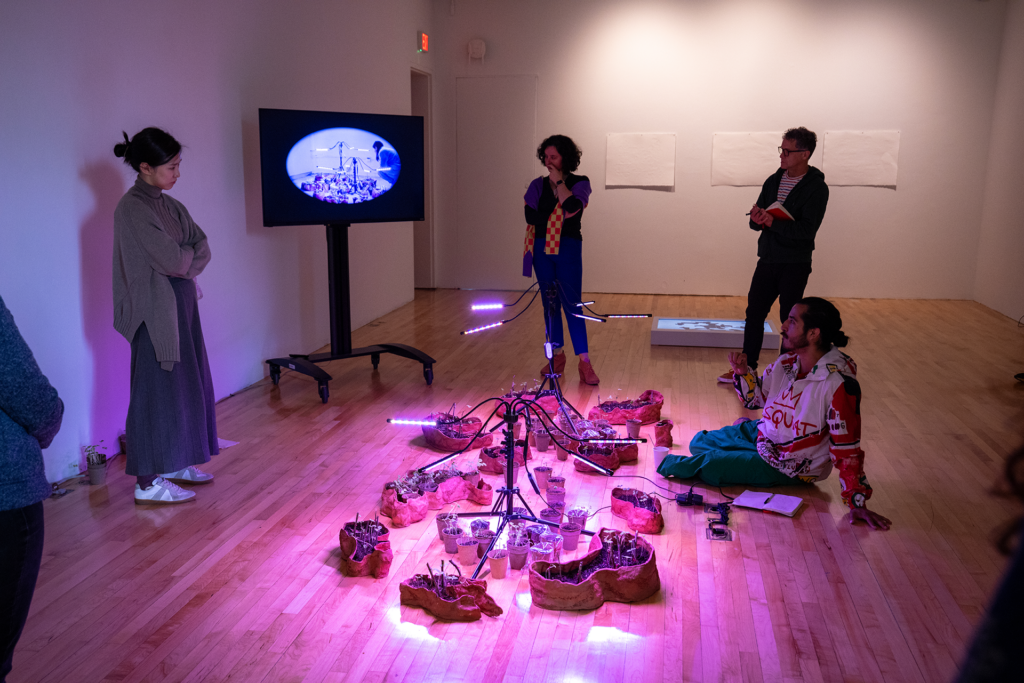 People standing and sitting on the floor looking at an art piece bathed in pink light.