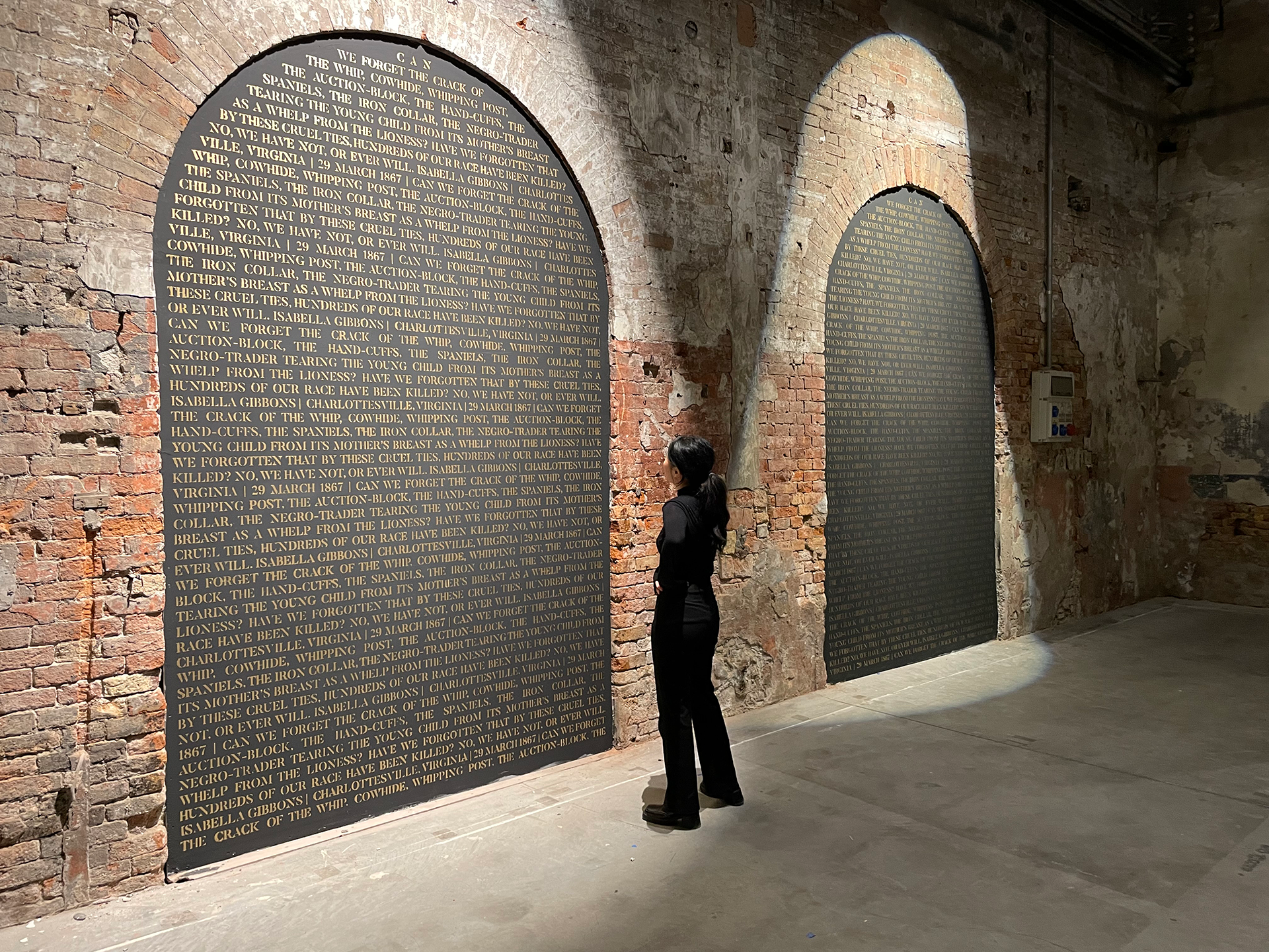 Person looking at a wall of names written on a black backdrop within a brick archway