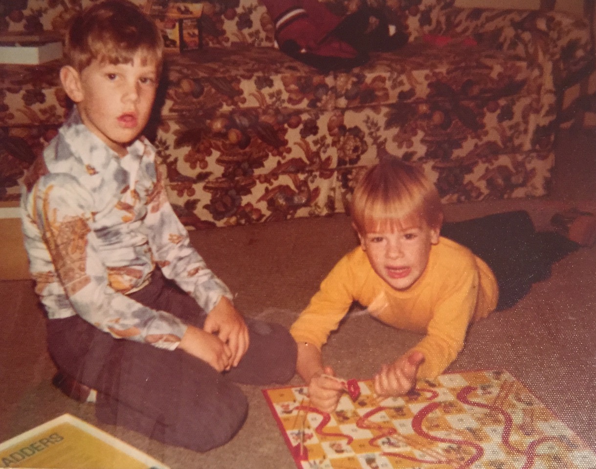 Two children sitting on brown carpet playing Chutes and Ladders