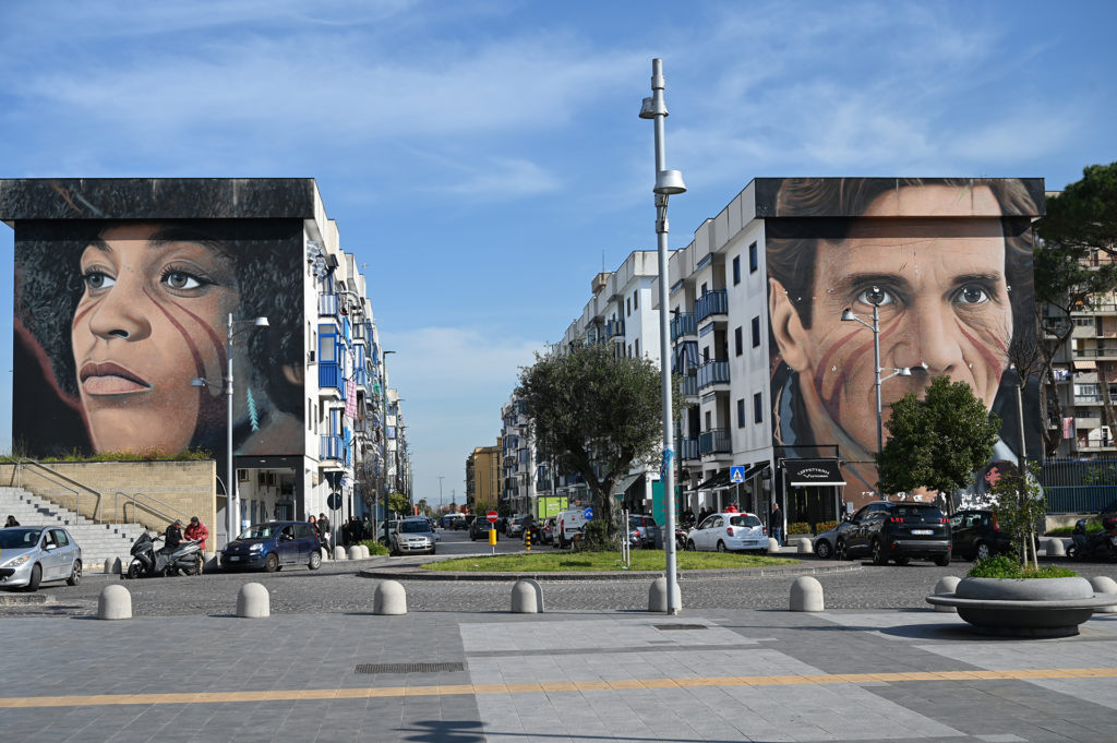 Murals painted on the side of buildings, one of a black woman and the other of a white man.