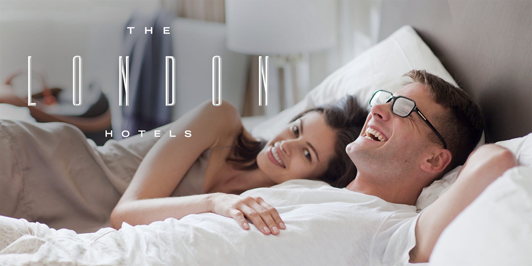 An ad for The London Hotels depicts a man and a woman happily lying in a bed