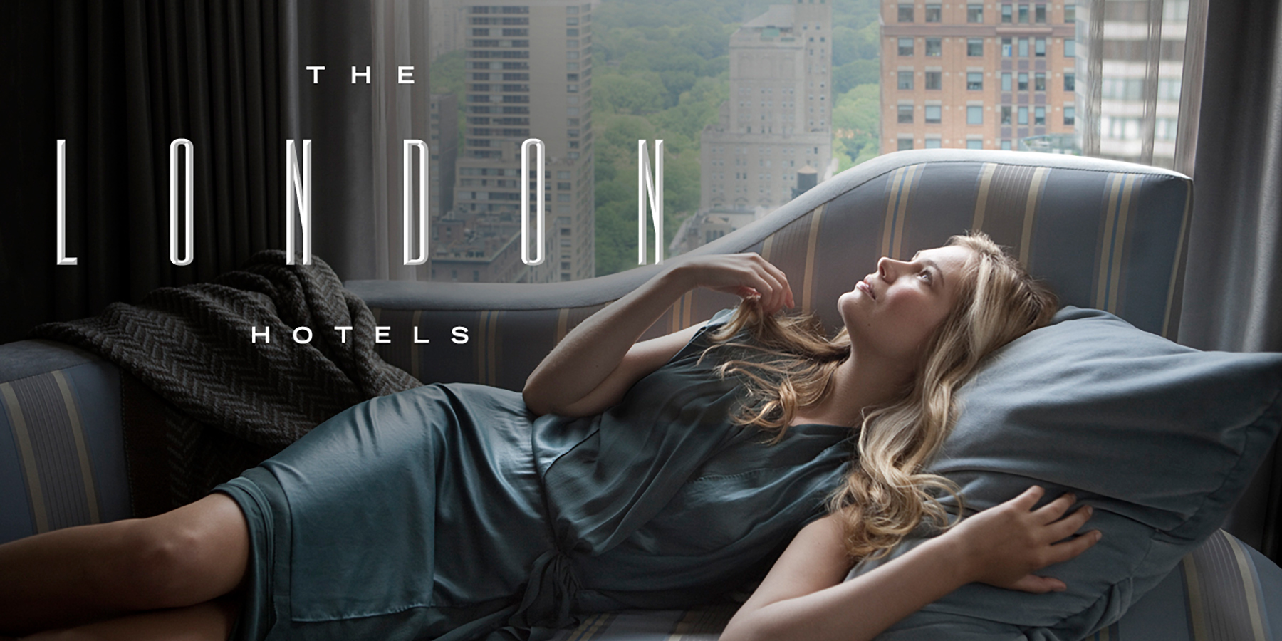 A blonde woman in a blue dress lies on a powder blue chaise, resting her head on a large blue pillow