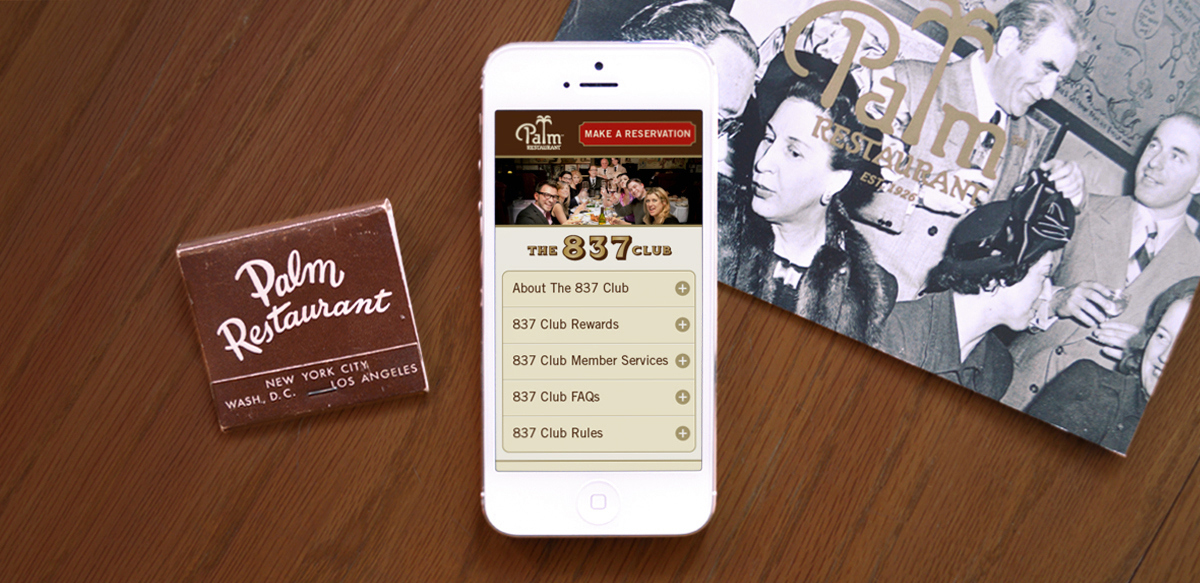 Palm Restaurant matches, a smartphone showing the Palm's mobile website, and a black-and-white photo lie on a wooden tabletop