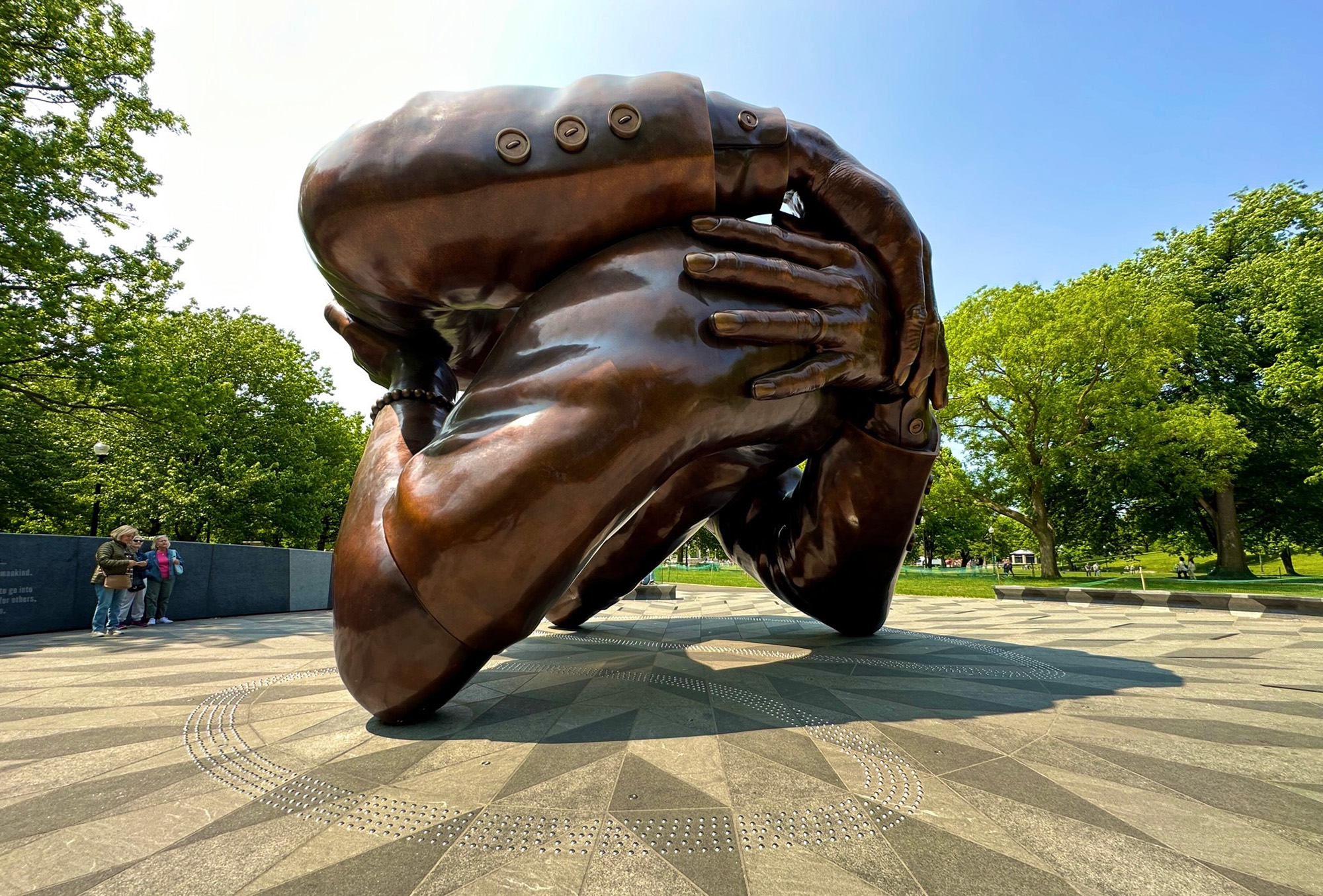 A large, bronze-colored outdoor monument depicts the arms of a couple embracing