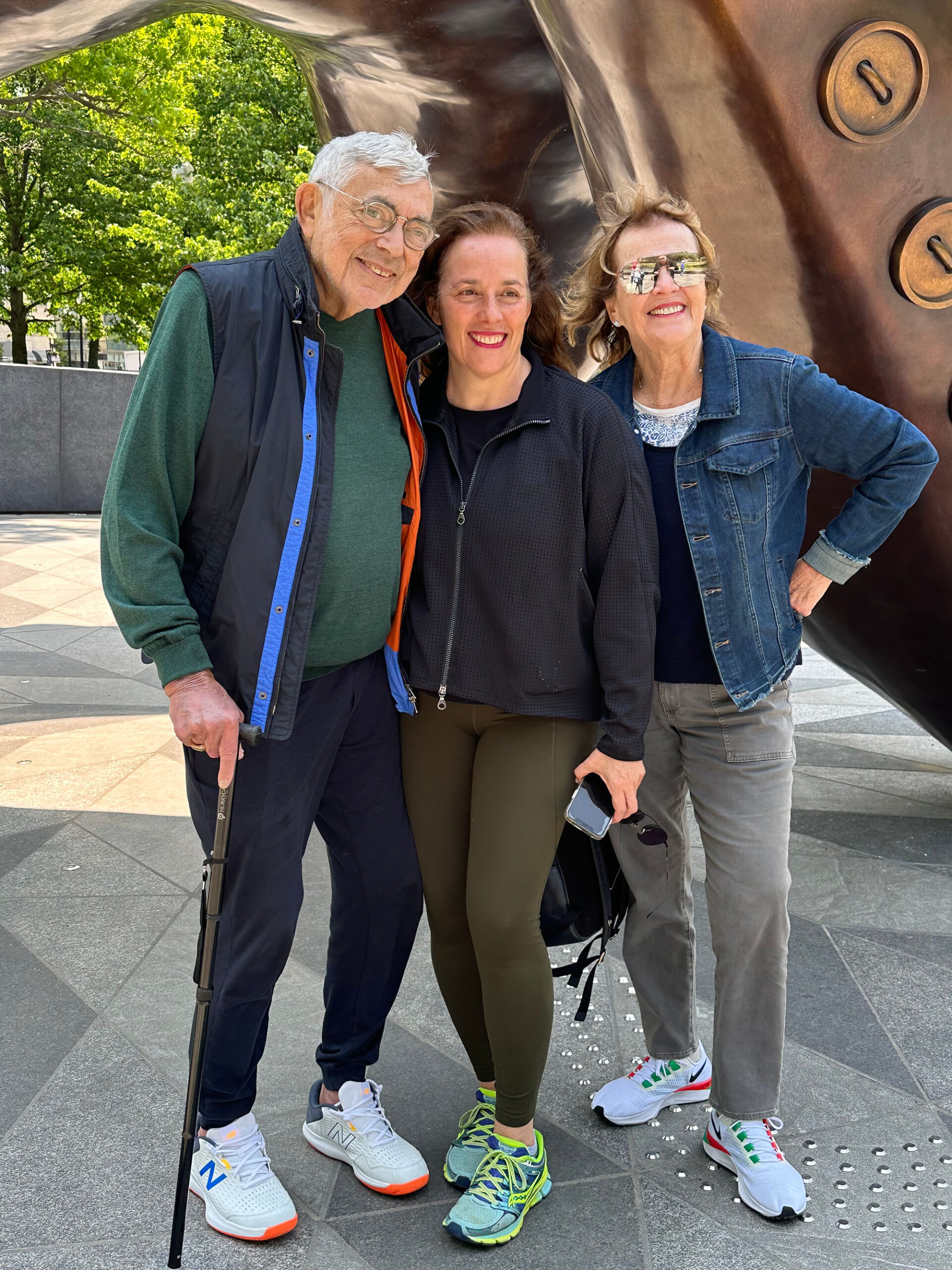 An elderly couple pose with their adult daughter in front of an outdoor monument