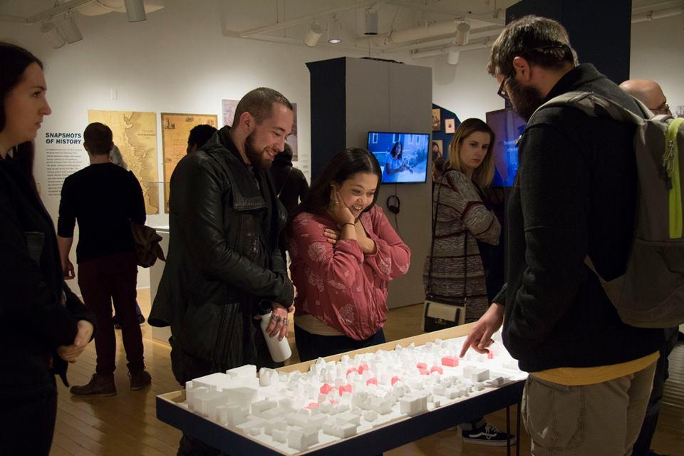 People looking at many architectural models on a table.