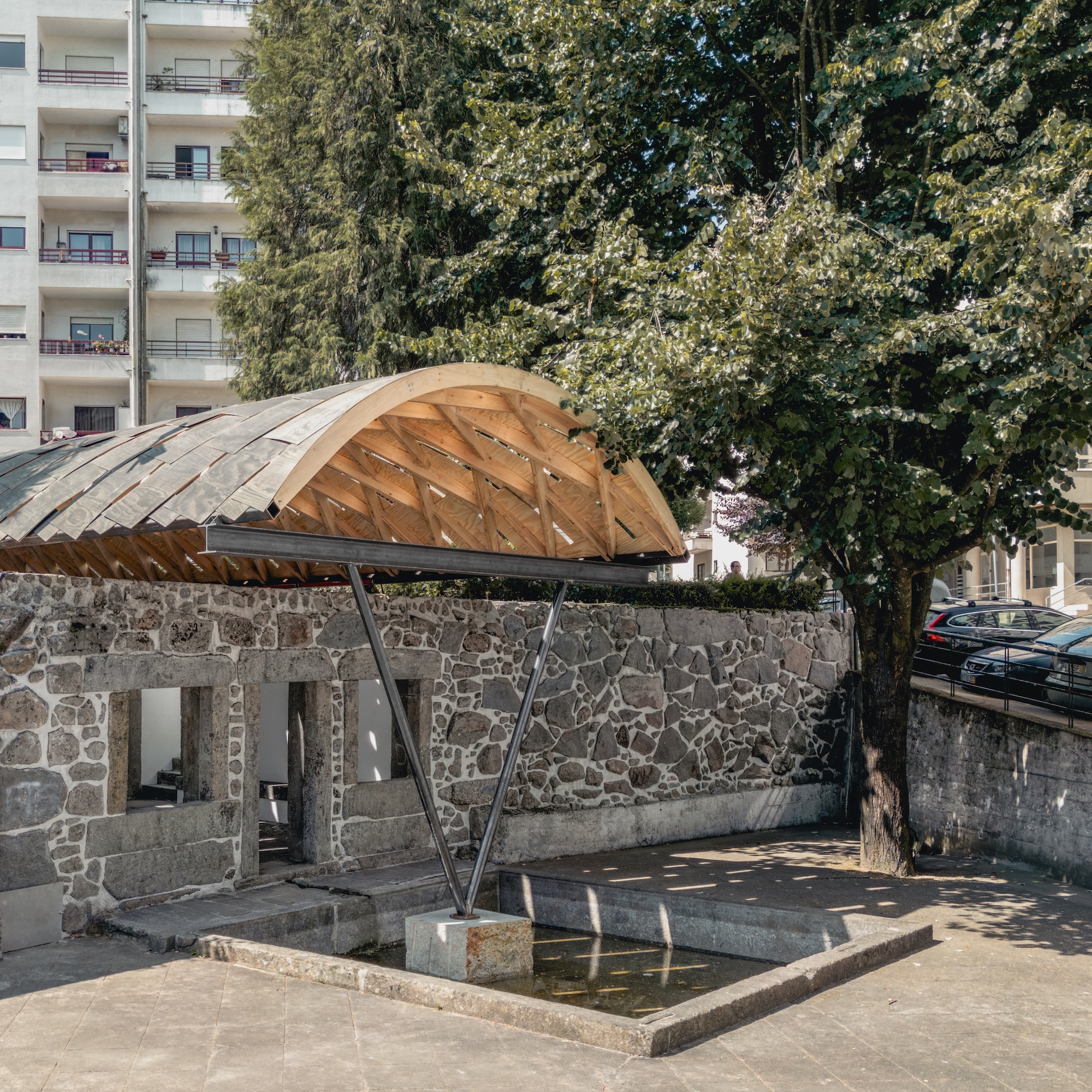 Stone building with a door and two windows overlooks a small concrete courtyard.