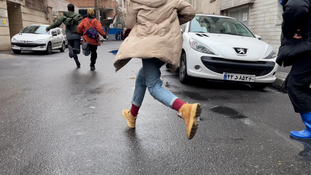 people running through a street between parked cars