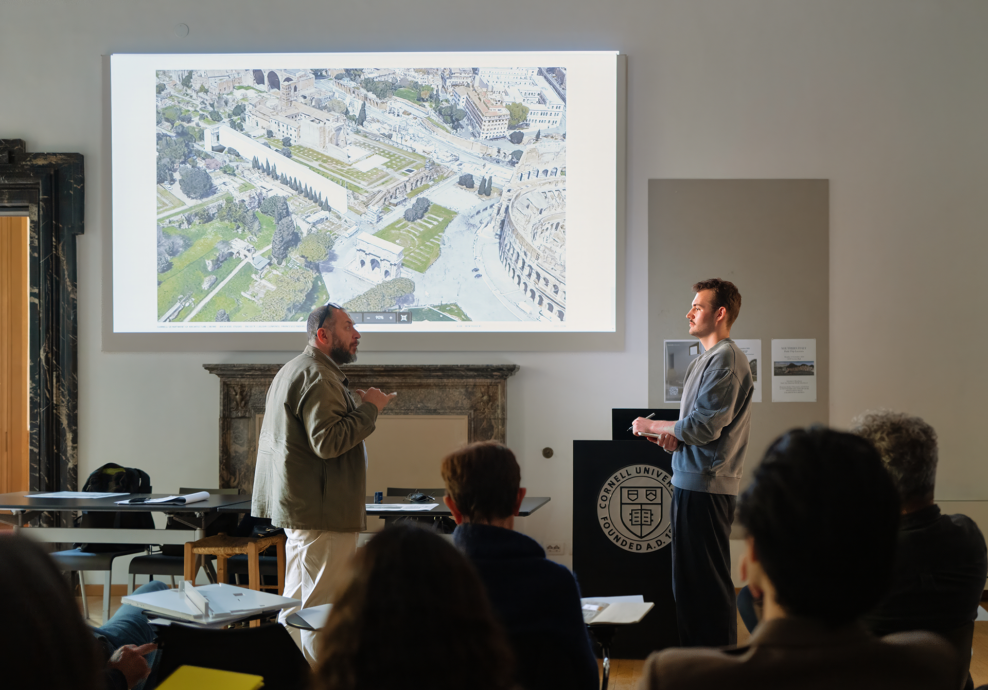 Student and teacher speaking in front of a screen projection in front of a class