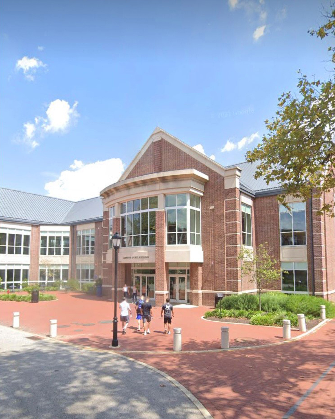 Students walk toward the entrance of a red brick building. Windows and tan trim break up the brick exterior.