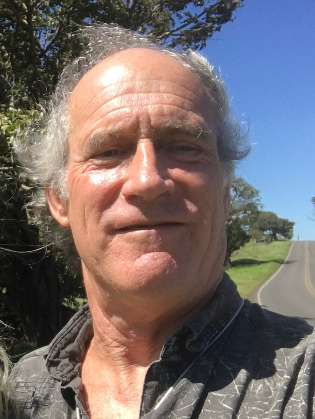 Photo taken outside of a man with light gray hair, wearing a gray shirt.